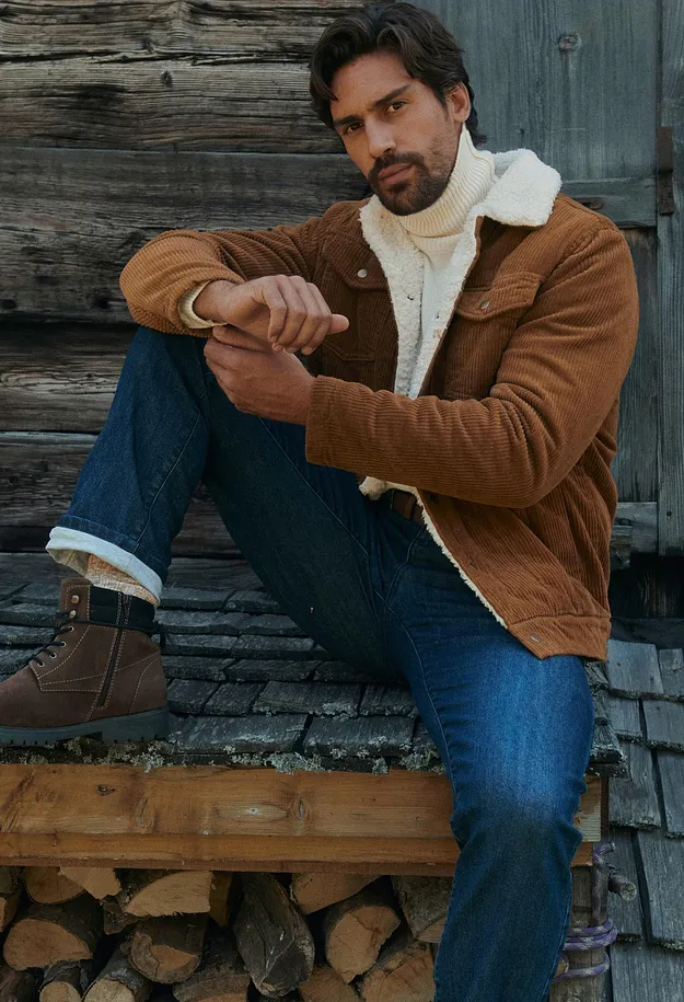 Una giacca di velluto a coste marrone, un maglione a collo alto bianco, jeans e stivali foderati caratterizzano l'outfit.