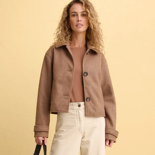 Elegante giacca corta marrone sopra un top delicato, abbinata a pantaloni chiari.