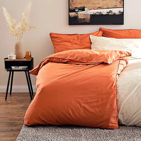 La biancheria da letto accogliente nei toni caldi dell'arancio e del crema invita al relax. 
