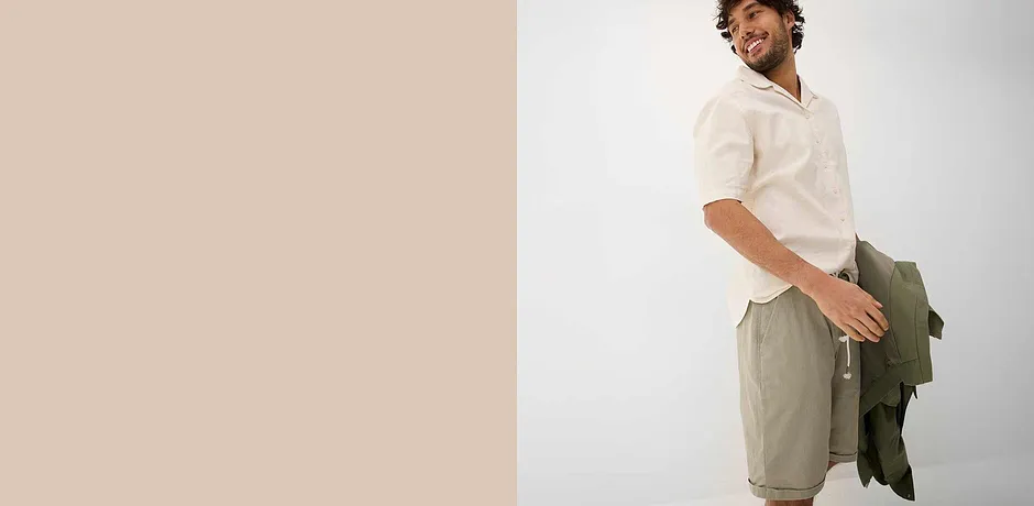 Camicia bianca leggera con colletto, pantaloncini beige e giacca verde per un look estivo rilassato. 
