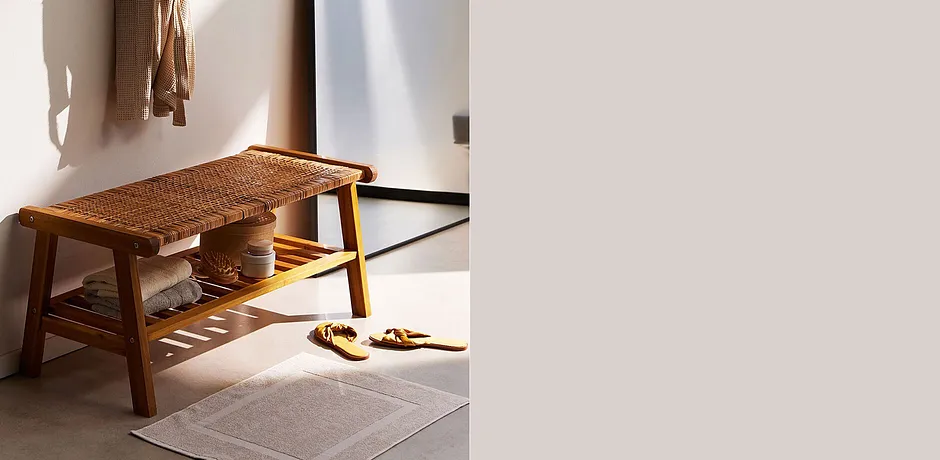 Accappatoio beige appeso al muro. Sotto, una panca con ciabattine estive.
