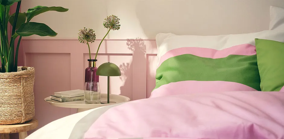 Biancheria da letto color pastello in rosa e verde decora il comodo letto in una camera da letto inondata di sole. 