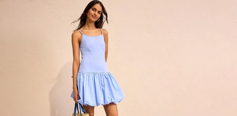 Abito estivo azzurro con sottili spalline e gonna svasata, abbinato a borsa di paglia. 