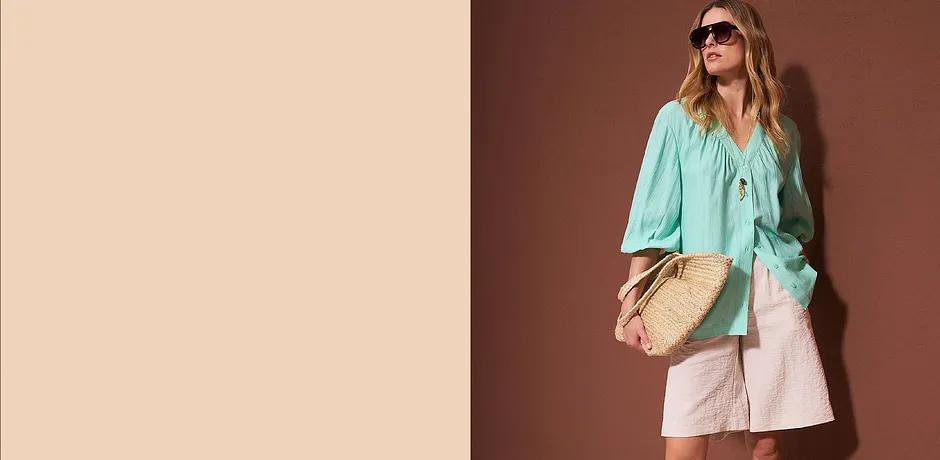 Blusa turchese, pantaloncini chiari e borsa di paglia. 