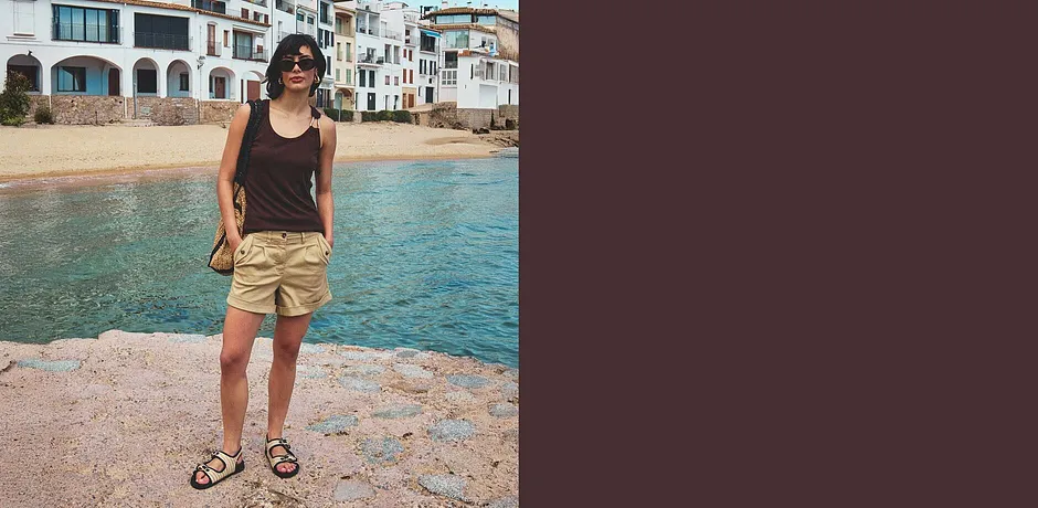 Donna con canotta marrone scuro e shorts beige abbinati a sandali in spiaggia.