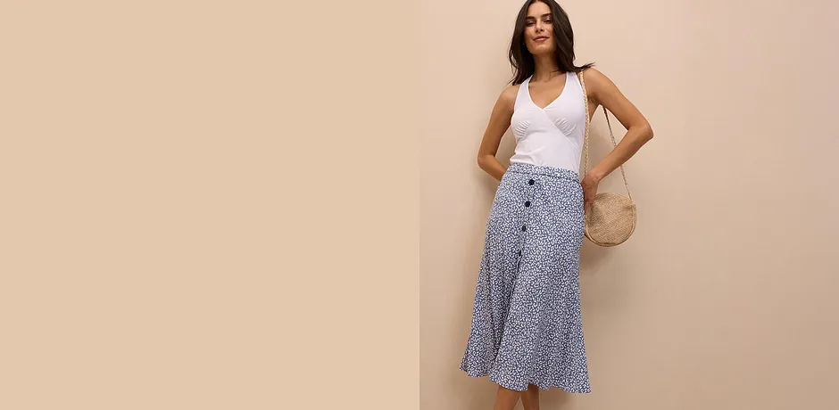 Top bianco senza maniche abbinato a una gonna midi a fantasia. A completare, una borsa di paglia per un tocco chic estivo.