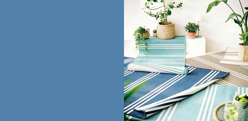 Tappeti da esterno a righe nei toni del blu e del verde decorano il tavolo, circondati da piante fresche.