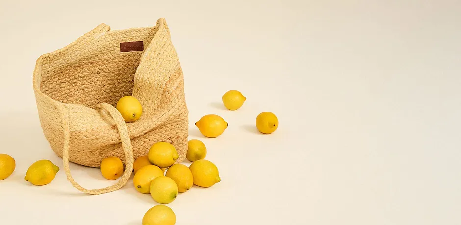 Borsa in rafia intrecciata con manici, piena di limoni freschi.