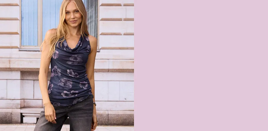 Top floreale grigio con scollo a cascata su jeans grigi.