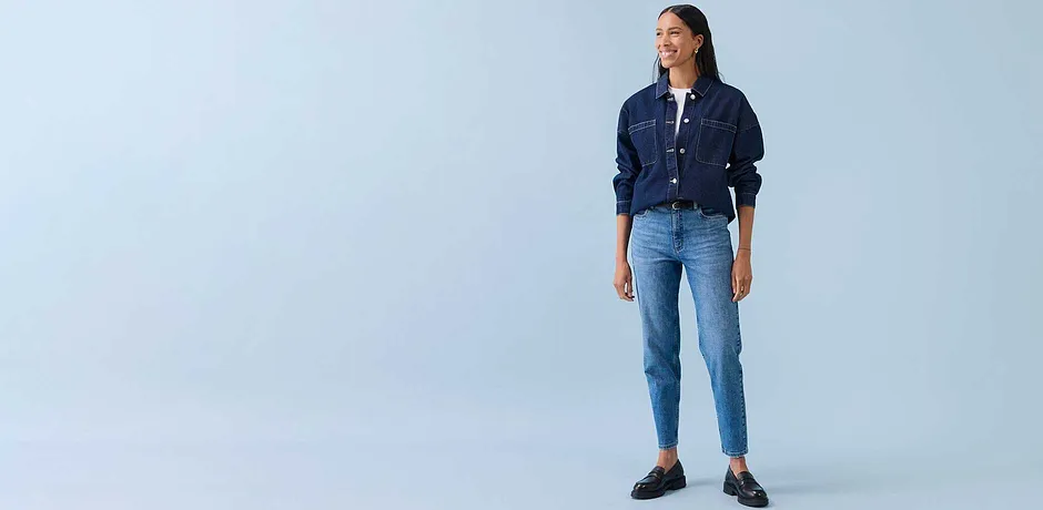 Look casual con giacca di jeans, camicia bianca e jeans azzurri. Scarpe scure completano l'outfit.