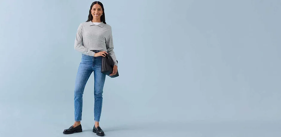 Felpa grigio chiaro, jeans skinny blu, ballerine scure e una borsa a tracolla marrone.