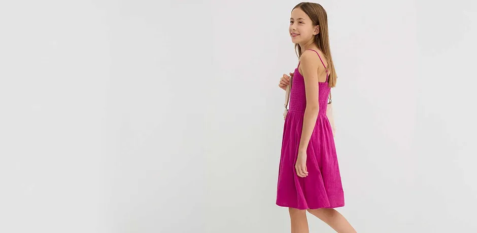 Abito fucsia in mussola con spalline sottili, abbinato a borsetta bianca.