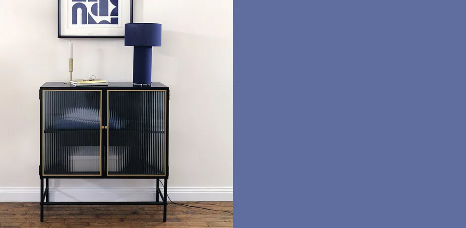 Elegante lampada da tavolo blu su un armadio nero con ante in vetro, sotto tessuti bianchi piegati.