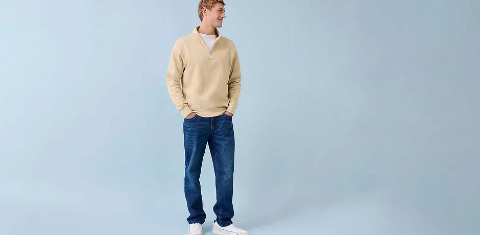 Look casual con maglione color crema, jeans blu e sneakers bianche.
