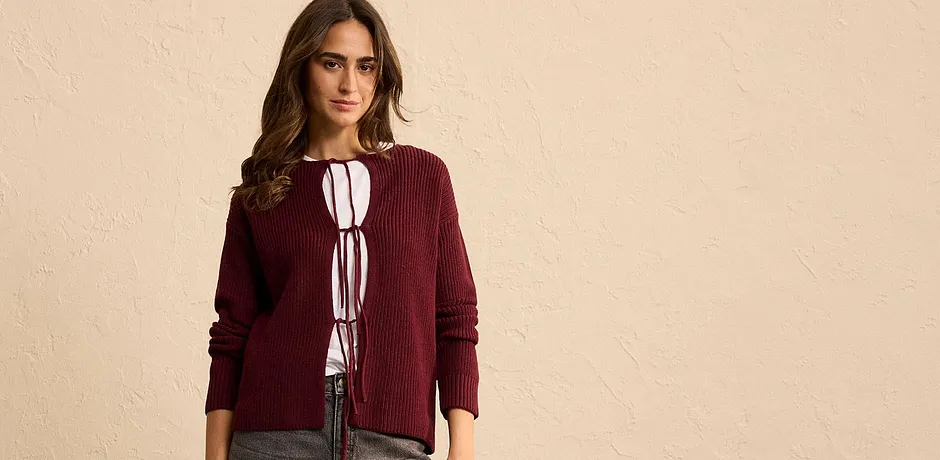 Cardigan bordeaux con fiocchi sopra una blusa bianca.