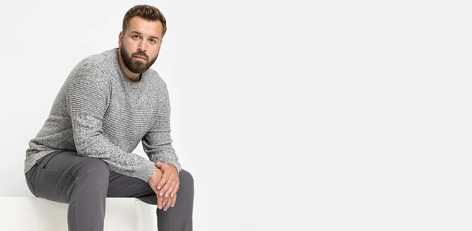 Un maglione grigio lavorato e pantaloni grigi creano un outfit casual.