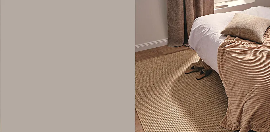 Comode pantofole poggiate su un tappeto in sisal naturale accanto a un letto con coperta a righe. 
