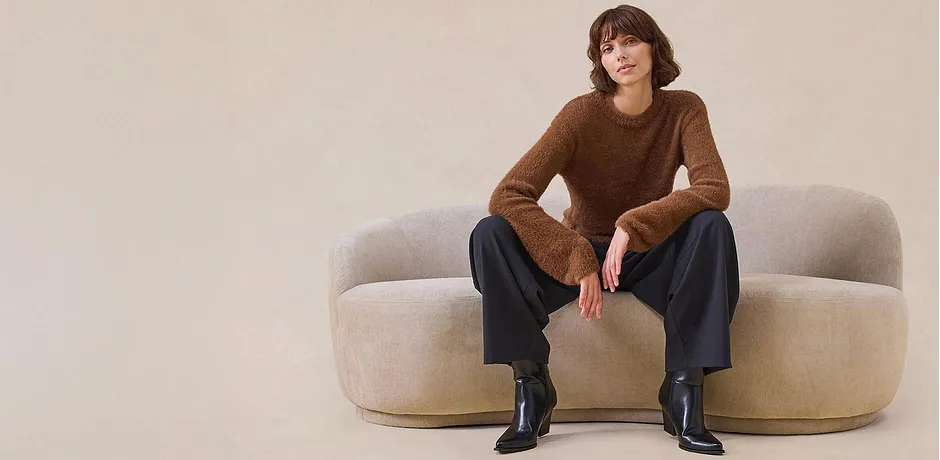 Elegante maglione marrone, pantaloni larghi e stivali neri.