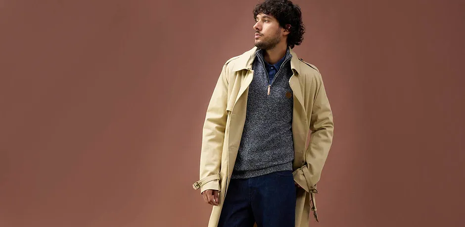 Trench beige su maglione blu-grigio e jeans: un look autunnale casual per le giornate fresche.