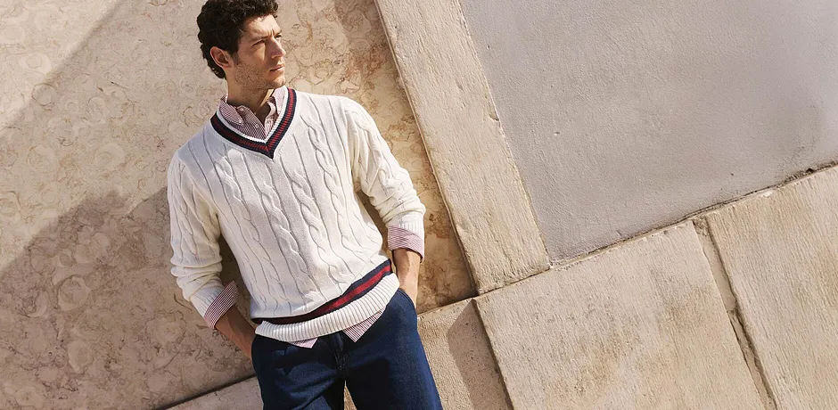 Elegante maglione con motivo a treccia e righe a contrasto, abbinato a una camicia classica e jeans scuri.