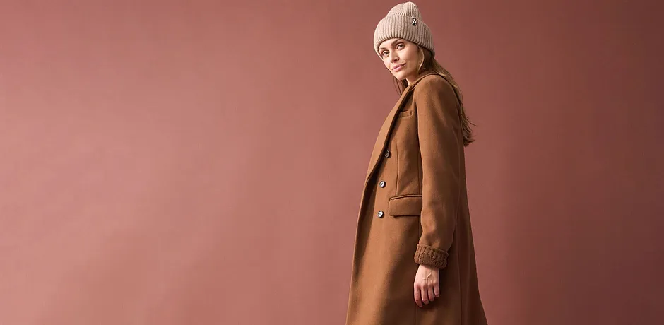 Cappotto lungo color cammello, berretto di maglia beige e abbigliamento semplice sotto.