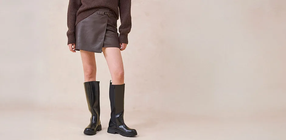 Gonna di pelle e stivali al ginocchio abbinati a un maglione marrone.