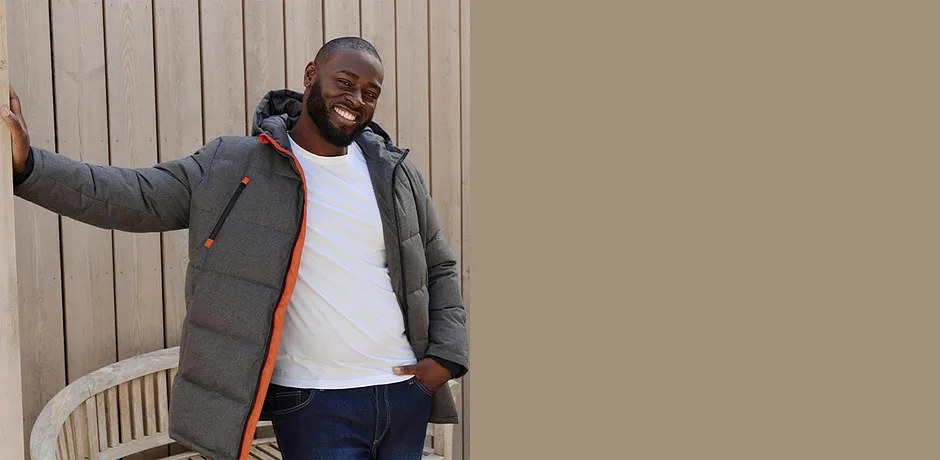 Grauer Winterjacke, weißes Shirt und dunkle Jeans prägen den lässigen Look.