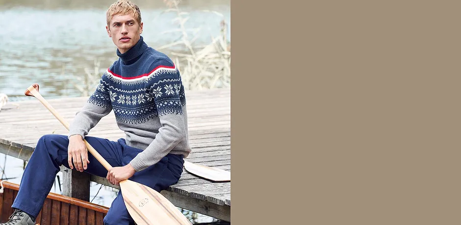 Un uomo con un maglione in fantasia norvegese e jeans è seduto rilassato su una barca.