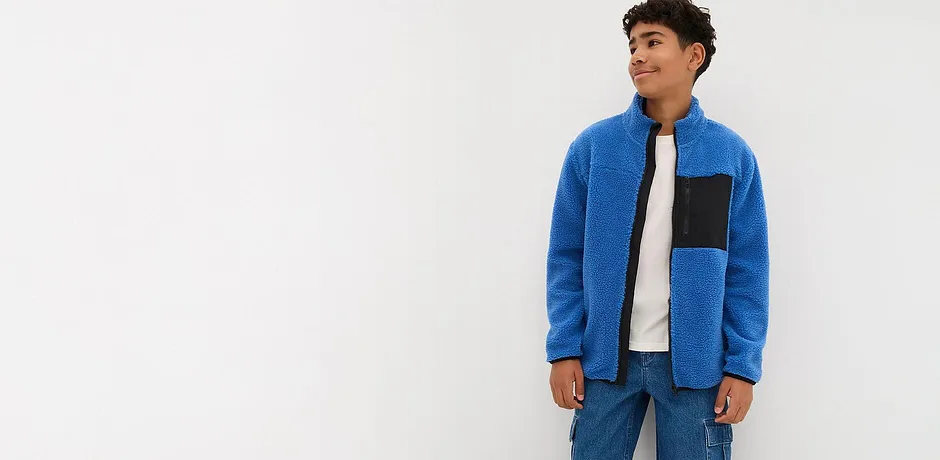 Un maglione blu in pile con inserto nero, abbinato a jeans e maglietta bianca.