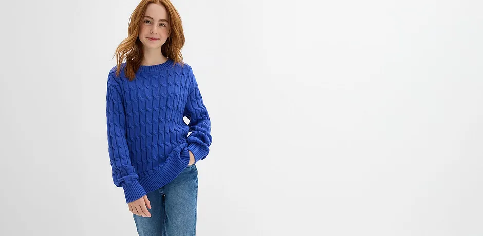 Maglione blu con motivo a trecce, abbinato a jeans classici per un look casual.