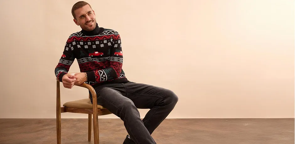 Maglione natalizio con motivi colorati, abbinato a jeans scuri. 