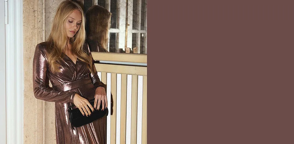 Abito scintillante con scollo a V abbinato a una borsa nera.