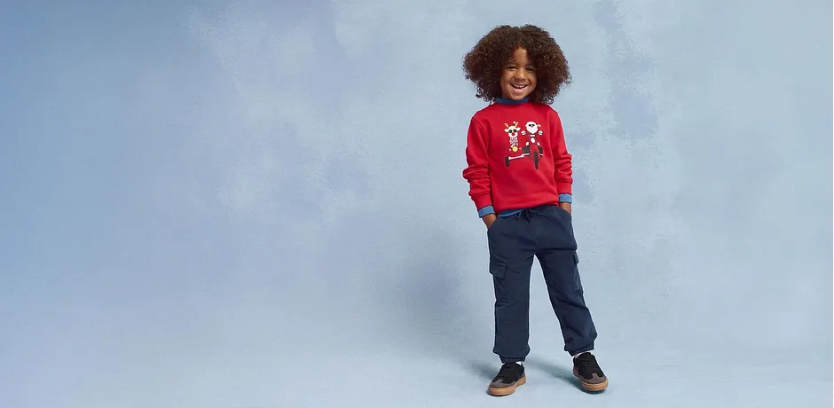 Maglione rosso con motivo natalizio, jeans blu e scarpe marroni.