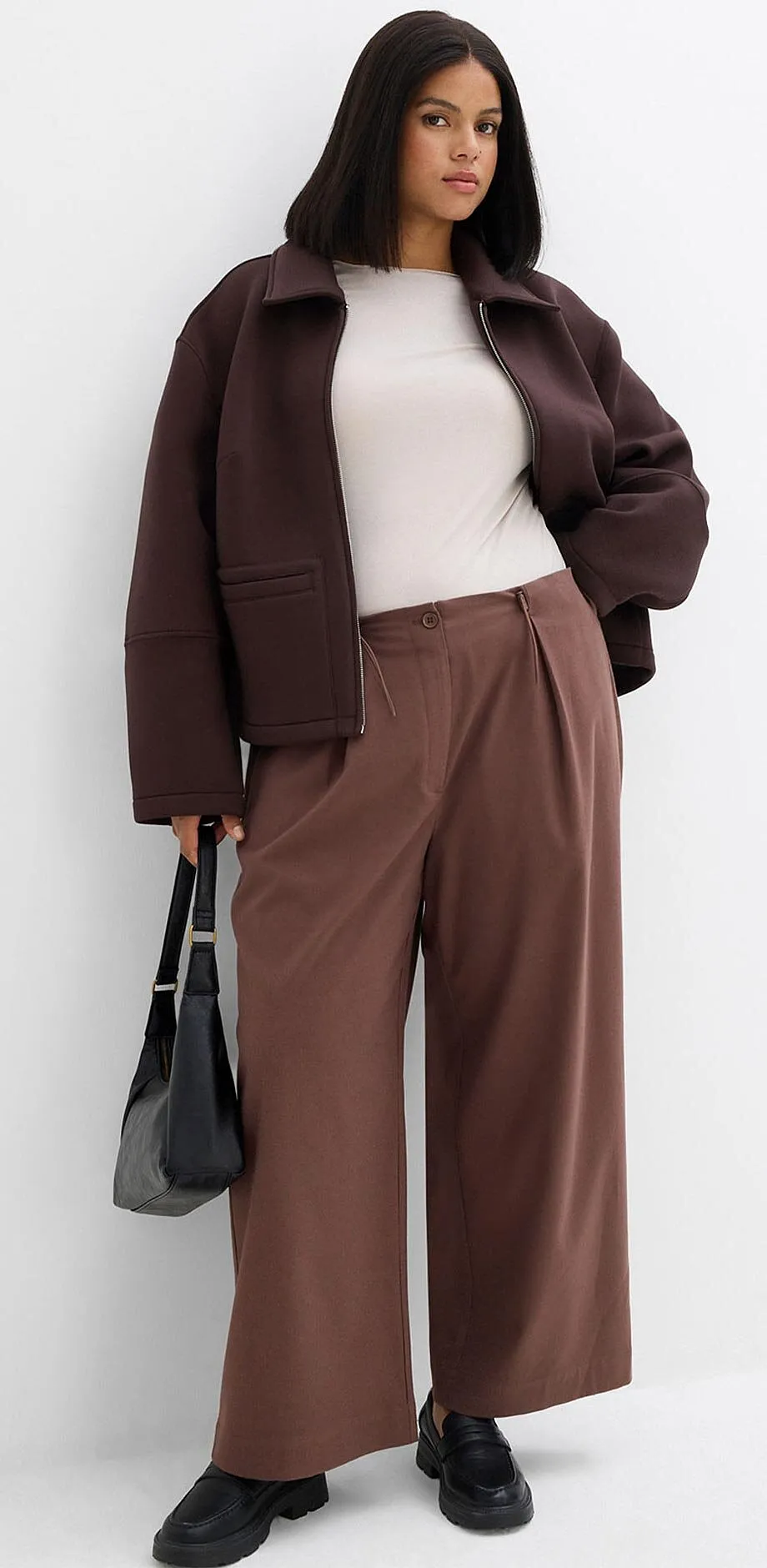 Giacca marrone, top bianco e pantaloni larghi nei toni della terra.