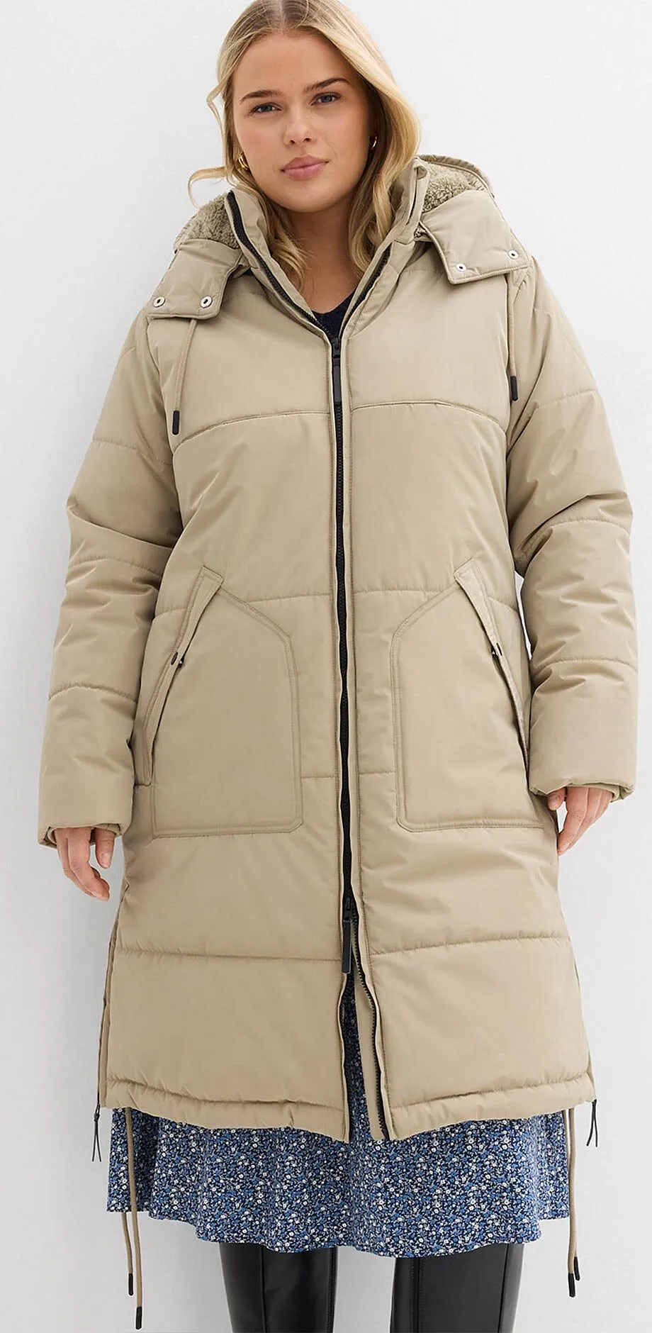 Giubbotto trapuntato beige con cappuccio sopra un abito blu a fiori. 