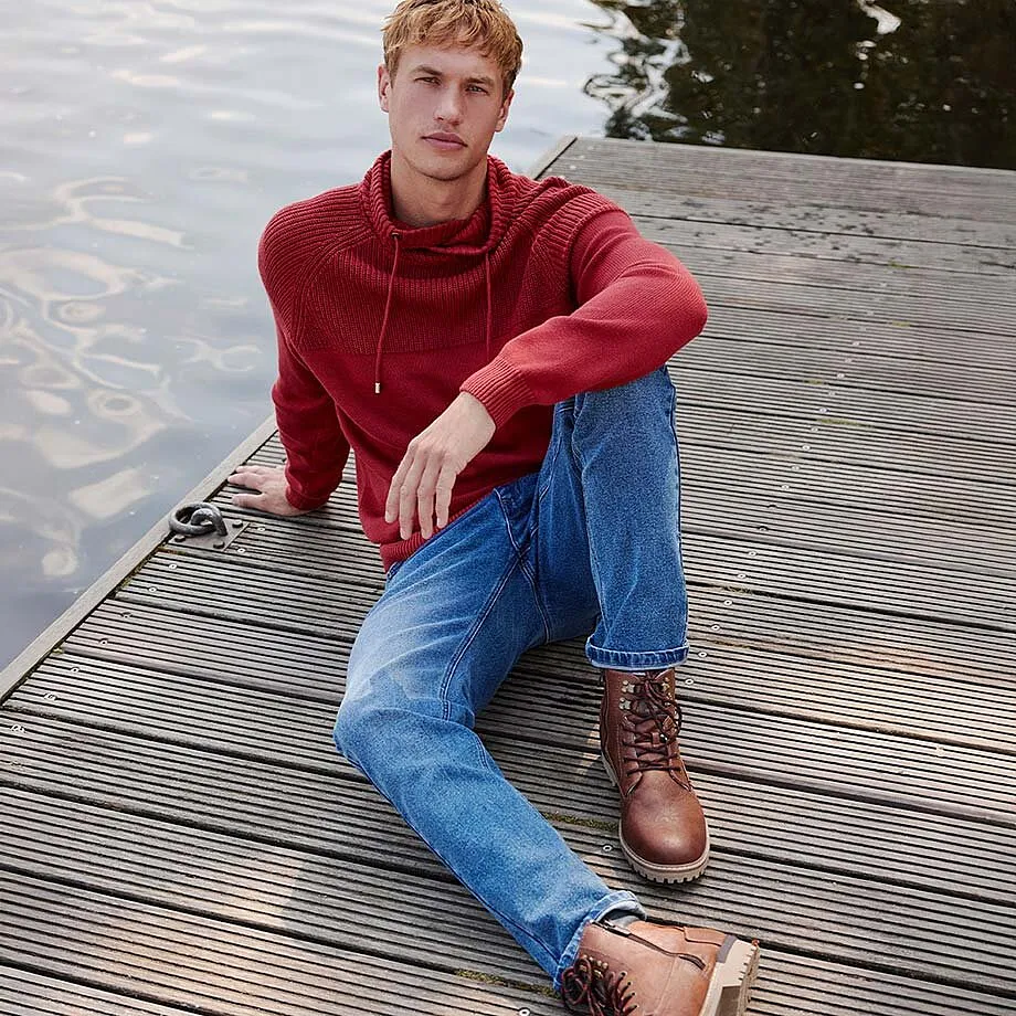 Felpa rossa con cappuccio abbinata a jeans blu e stivali di pelle marroni.