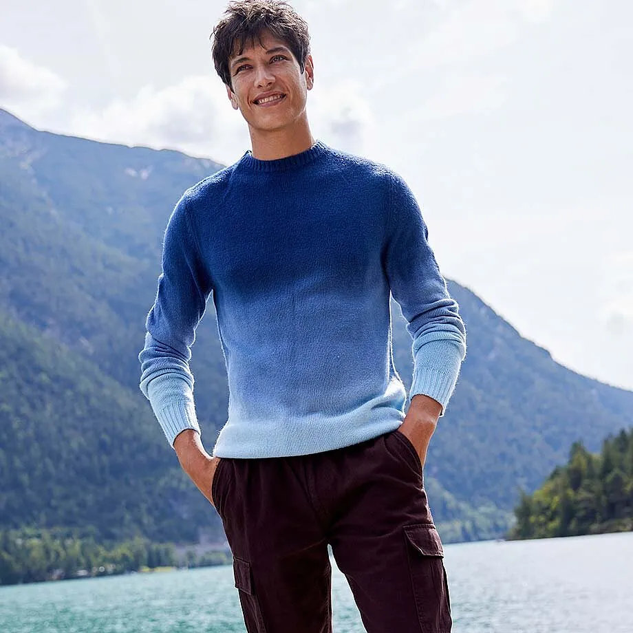 Un maglione blu sfumato e pantaloni cargo scuri creano un outfit casual.