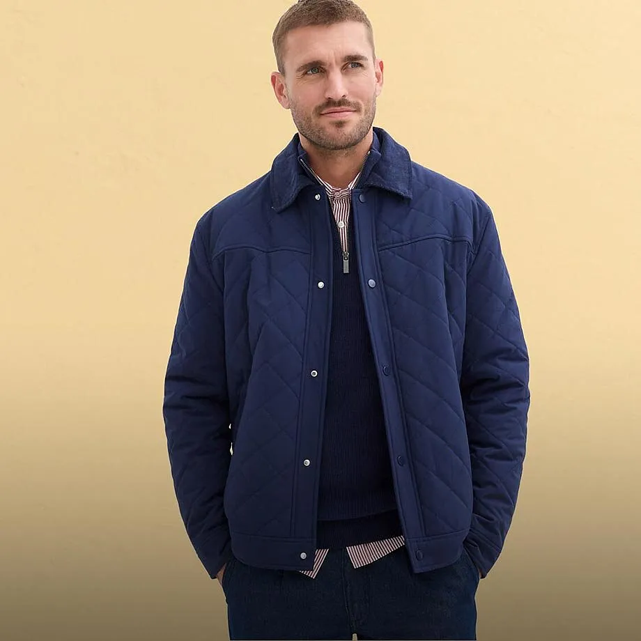 Giacca trapuntata blu-grigia, maglietta chiara, jeans e cappellino da baseball bianco.