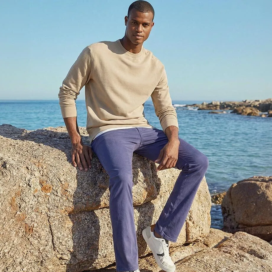 Il maglione beige e i pantaloni viola si armonizzano perfettamente con lo sfondo marino.