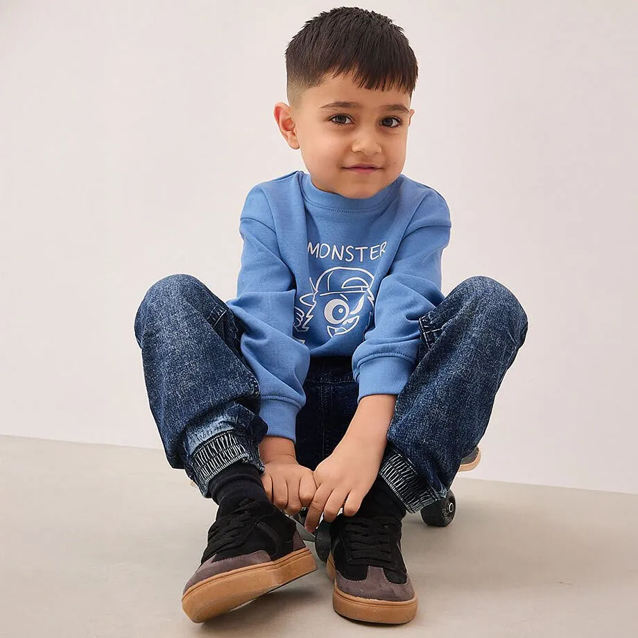 Felpa blu con mostriciattolo stampato, jeans scuri e scarpe da ginnastica nere.