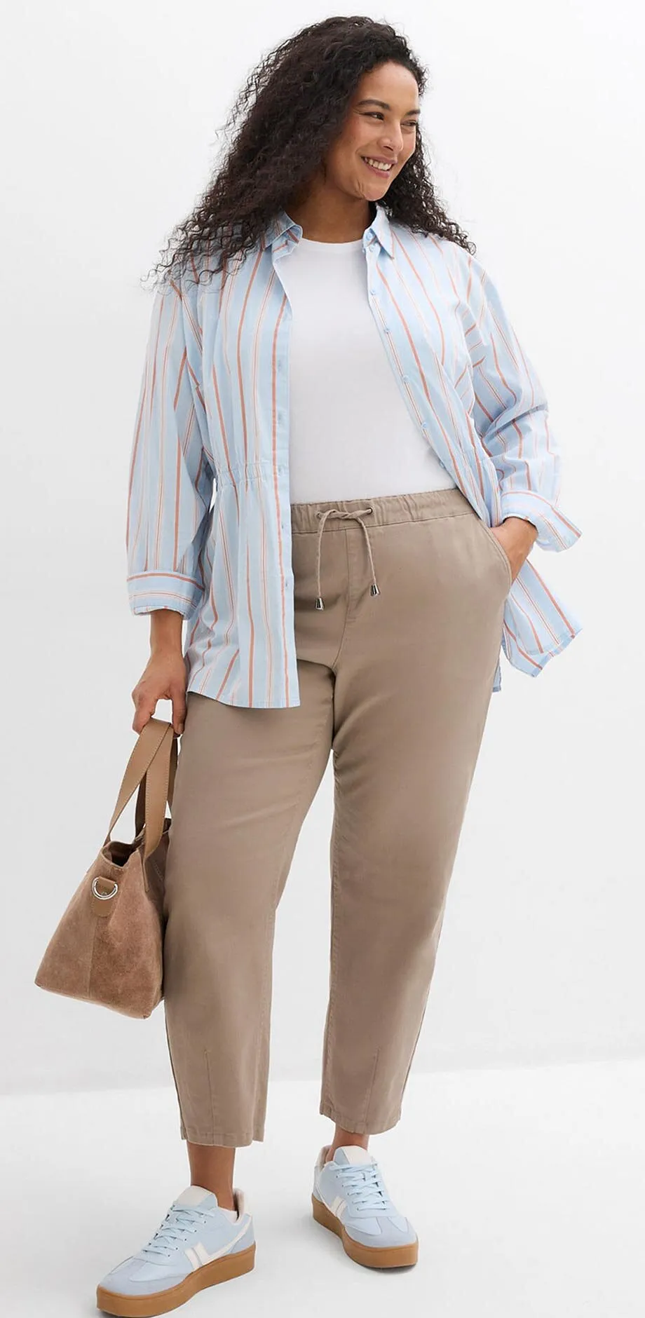 Camicia a righe sopra una maglietta bianca, pantaloni beige e scarpe da ginnastica azzurre.