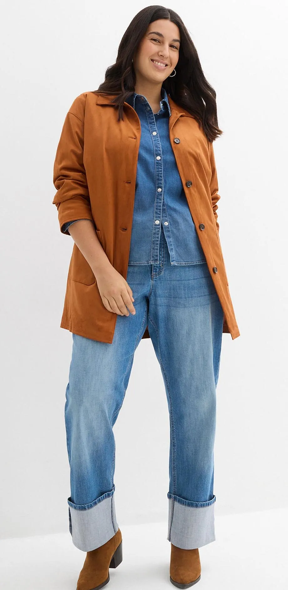 Giacca marrone sopra camicia di jeans e jeans larghi con risvolto.