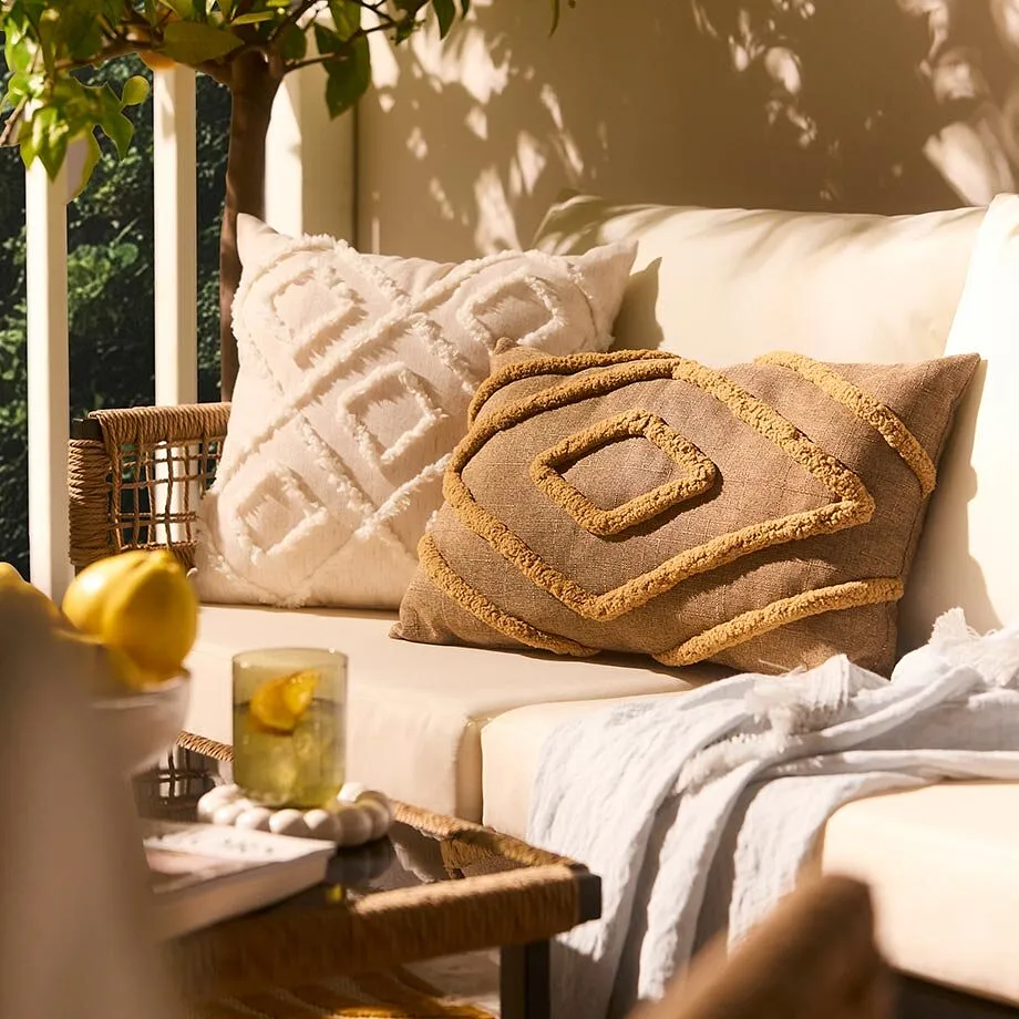 Accogliente salotto all'aperto con cuscini chiari e morbida coperta. 