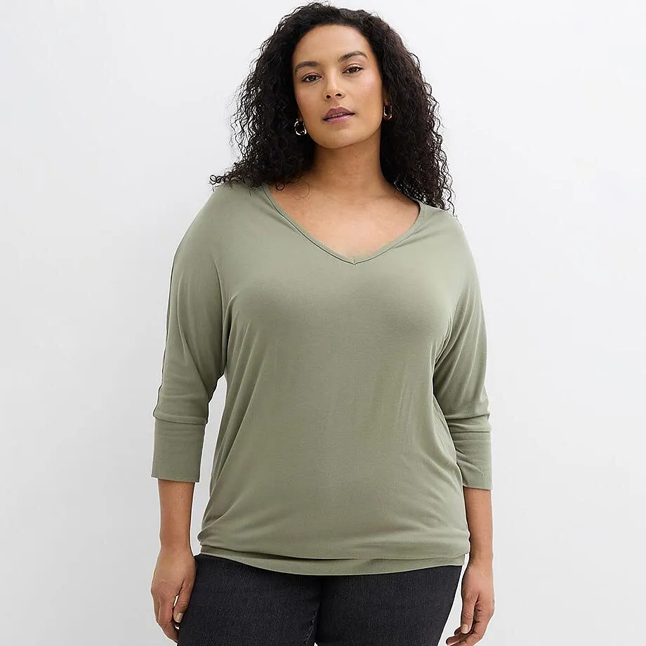 Look disinvolto con maglietta verde salvia con scollo a V e jeans scuri.