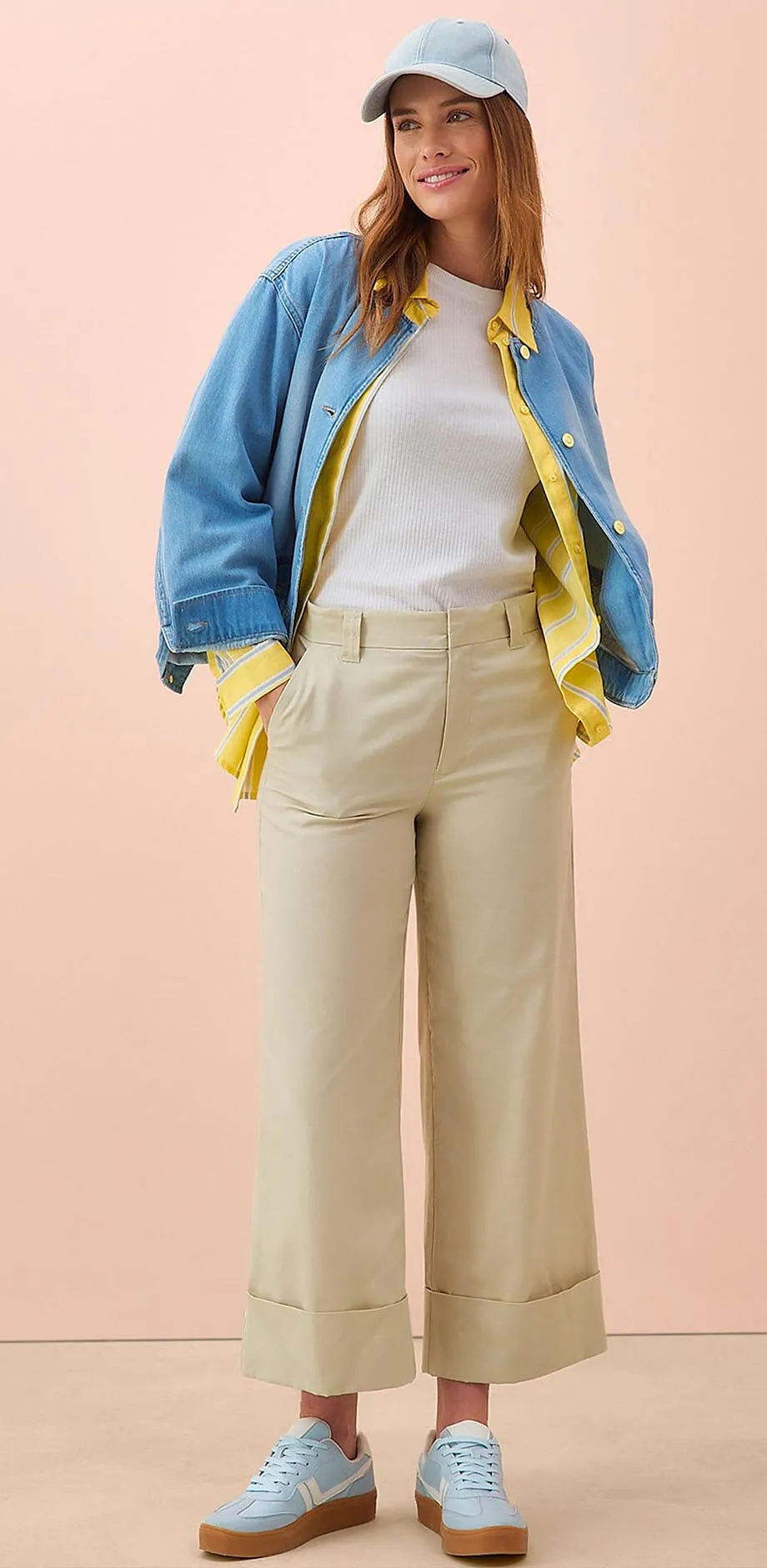 Outfit primaverile con giacca di jeans, maglia bianca, pantaloni culotte beige e sneaker azzurre.