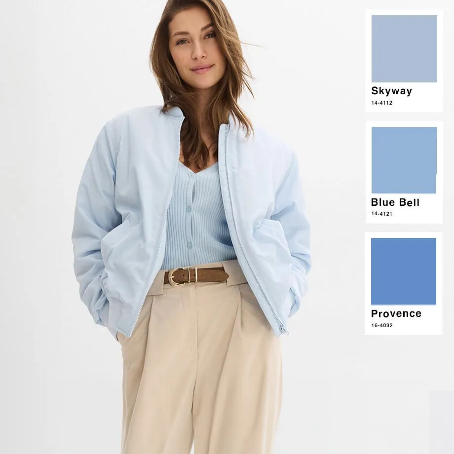 Bomber azzurro sopra un top azzurro, pantaloni beige con cintura marrone. Un look primaverile disinvolto.