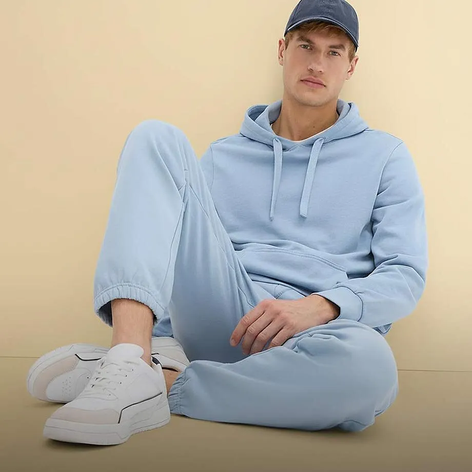 Felpa con cappuccio azzurra e pantaloni da jogging, completati da scarpe da ginnastica bianche e un berretto blu.