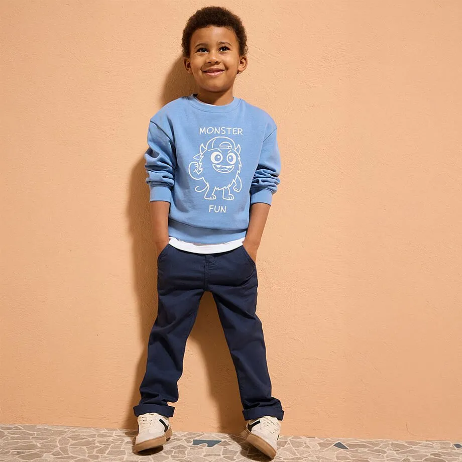 Una felpa azzurra con una stampa bianca, jeans scuri e scarpe beige creano un outfit casual.