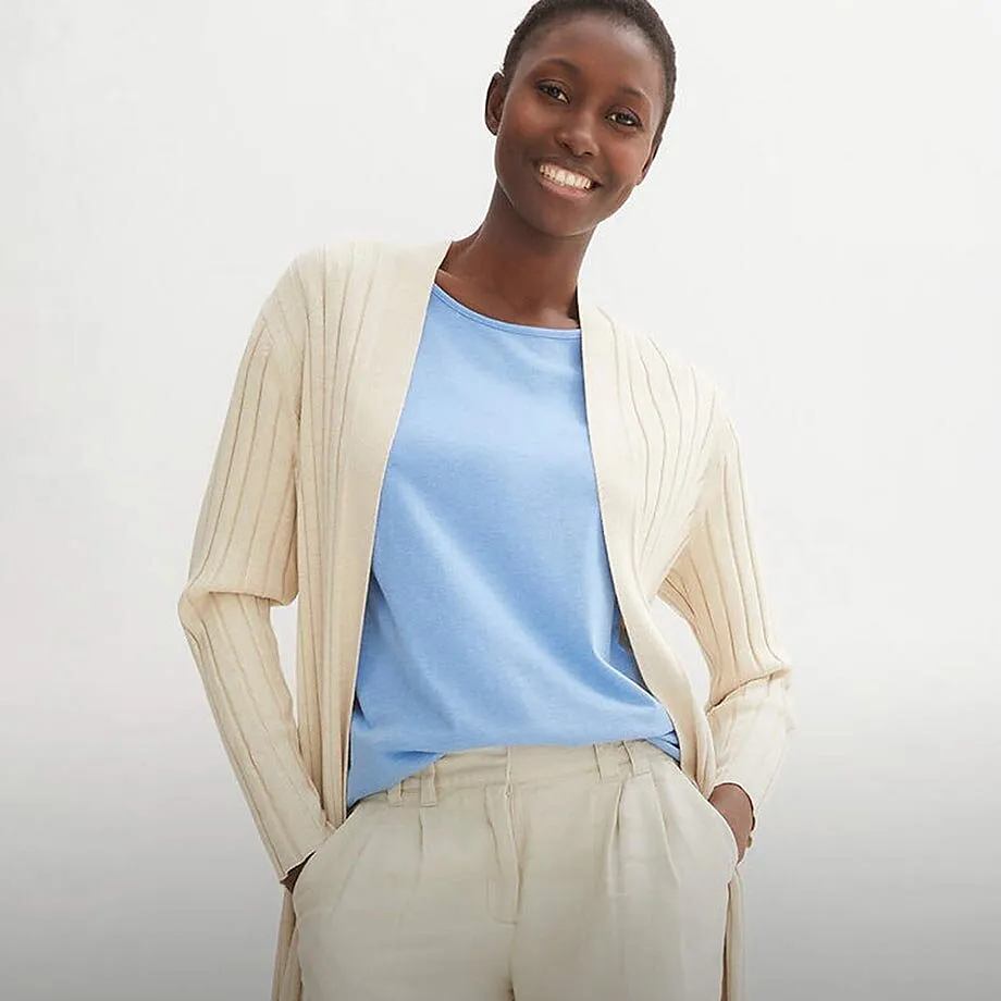 Cardigan color crema sopra una maglia azzurra, abbinato a pantaloni da completo chiari.