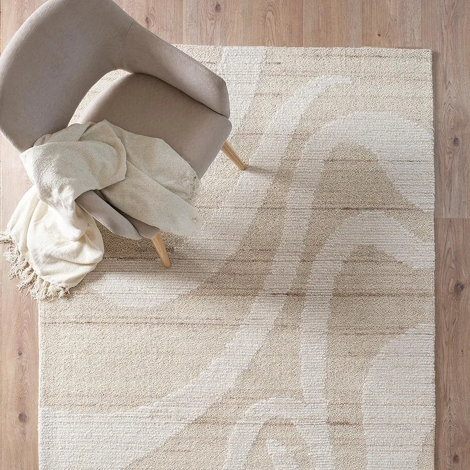 Elegante tappeto color crema con motivi discreti, su cui poggiano una comoda poltrona e una morbida coperta.